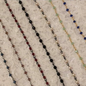 Puede incluir: Una variedad de delicados collares de cuentas en varios colores. Los collares presentan pequeñas cuentas en tonos azul, marrón, rojo, negro, blanco, verde y azul, ensartadas en finas cadenas. Las cadenas son doradas y negras.