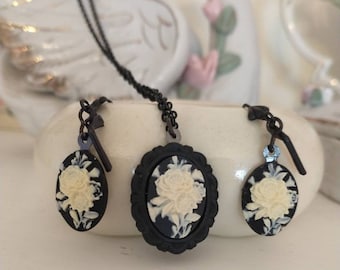 May include: A black cameo necklace and earrings set with a white floral design. The necklace has a black chain and the earrings have black hooks.