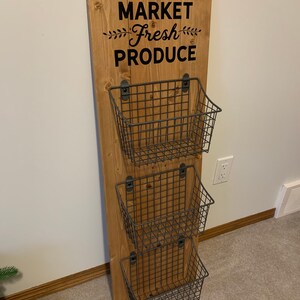 May include: A wooden wall-mounted organizer with the text "MARKET Fresh PRODUCE" and three wire baskets.