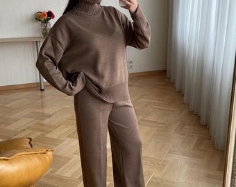 May include: A matching two-piece set consisting of a brown long-sleeve sweater with a ribbed turtleneck and wide-leg trousers. The sweater features dropped shoulders and ribbed cuffs, while the trousers have a straight-leg cut and a smooth finish.