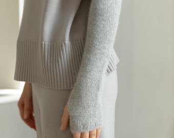 May include: A light gray long-sleeved sweater with a ribbed hem and cuffs, paired with a matching light gray knitted arm warmer that extends from the wrist to the mid-forearm, featuring a thumb hole and a soft, fuzzy texture.