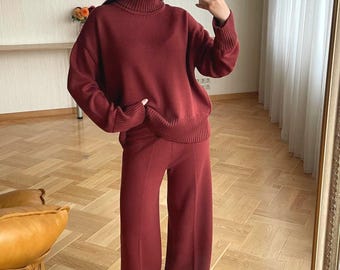 May include: A dark red knit two-piece set consisting of a long-sleeve sweater with a high turtleneck collar and matching wide-leg trousers. The sweater features ribbed cuffs and a ribbed hem, while the trousers have a straight-leg silhouette.