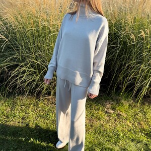 Peut inclure: Un ensemble assorti gris clair composé d'un pull à manches longues avec un col roulé montant et des poignets côtelés, associé à un pantalon large assorti doté d'une taille élastique à cordon de serrage et d'une texture en maille lisse.