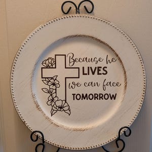 May include: White charger plate with a brown cross and floral design. The plate has the text "Because he LIVES we can face TOMORROW" on it.