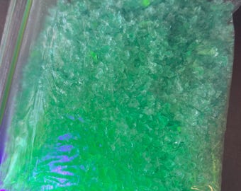 May include: A clear plastic bag filled with bright green crystal-like pieces. The bag is sealed with a zipper.