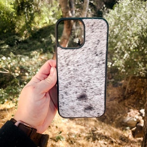 May include: A white and black cowhide phone case with a black border. The case is designed for a smartphone with a camera lens cutout.