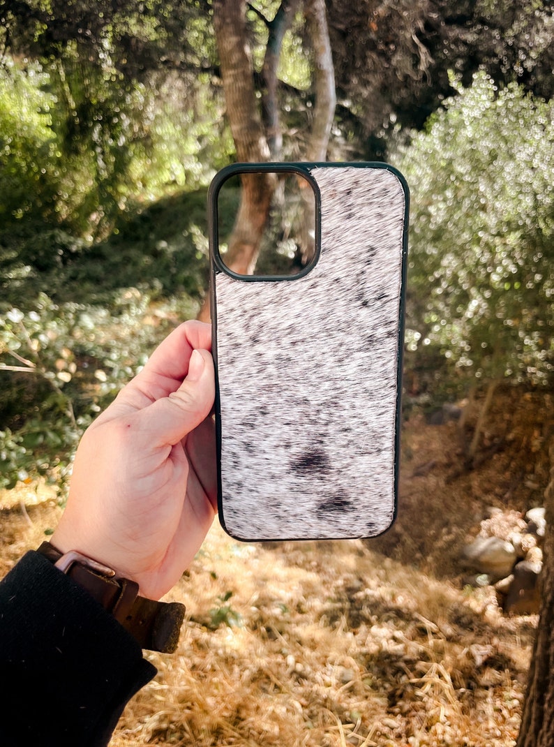 May include: A white and black cowhide phone case with a black border. The case is designed for a smartphone with a camera lens cutout.