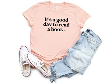 May include: A peach-coloured t-shirt with the text "It's a good day to read a book." printed in black. The shirt is paired with light blue denim jeans and white trainers.