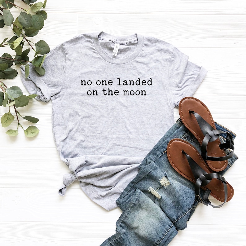 May include: A gray t-shirt with the text "no one landed on the moon" printed in black.
