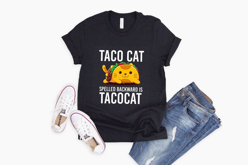 Puede incluir: Una camiseta negra con un gr&aacute;fico blanco de un gato con forma de taco. El texto en la camiseta dice "Taco Cat Spelled Backward is Tacocat."