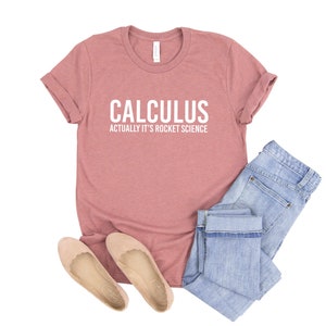May include: A dusty rose colored t-shirt with the text "CALCULUS ACTUALLY IT'S ROCKET SCIENCE" in white lettering.