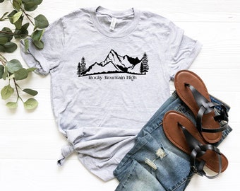 Op de afbeelding: Een grijs T-shirt met een zwart berg silhouet en de tekst "Rocky Mountain High" gedrukt op de voorkant.