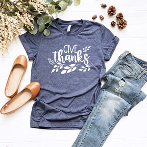 May include: A navy blue t-shirt with the text "GIVE THANKS" in white lettering with white leaf designs around the text.