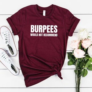 May include: A maroon t-shirt with the text "Burpees Would Not Recommend" in white lettering.