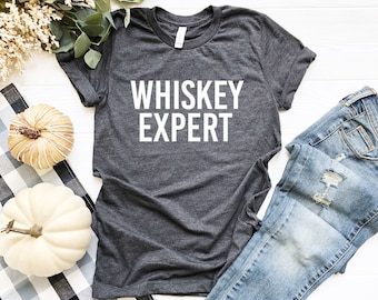 Peut inclure: Un t-shirt gris foncé avec le texte "WHISKEY EXPERT" imprimé en blanc sur le devant.