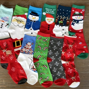 May include: A collection of 12 Christmas themed socks featuring various designs including Santa Claus, reindeer, snowmen, candy canes, and snowflakes. The socks are in a variety of colors, including red, green, blue, and white.