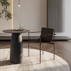 May include: A black metal chair with a black fabric seat sits next to a black round side table with a glass decanter and a tray on top. The table and chair are on a white rug in a room with light wood floors.