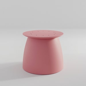 Pu&ograve; includere: Uno sgabello rotondo di colore rosa con una base leggermente svasata. La parte superiore dello sgabello ha un cerchio di piccoli fori.