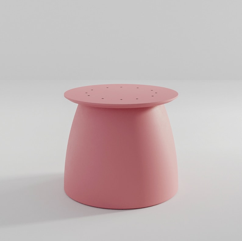 Pu&ograve; includere: Uno sgabello rotondo di colore rosa con una base leggermente svasata. La parte superiore dello sgabello ha un cerchio di piccoli fori.