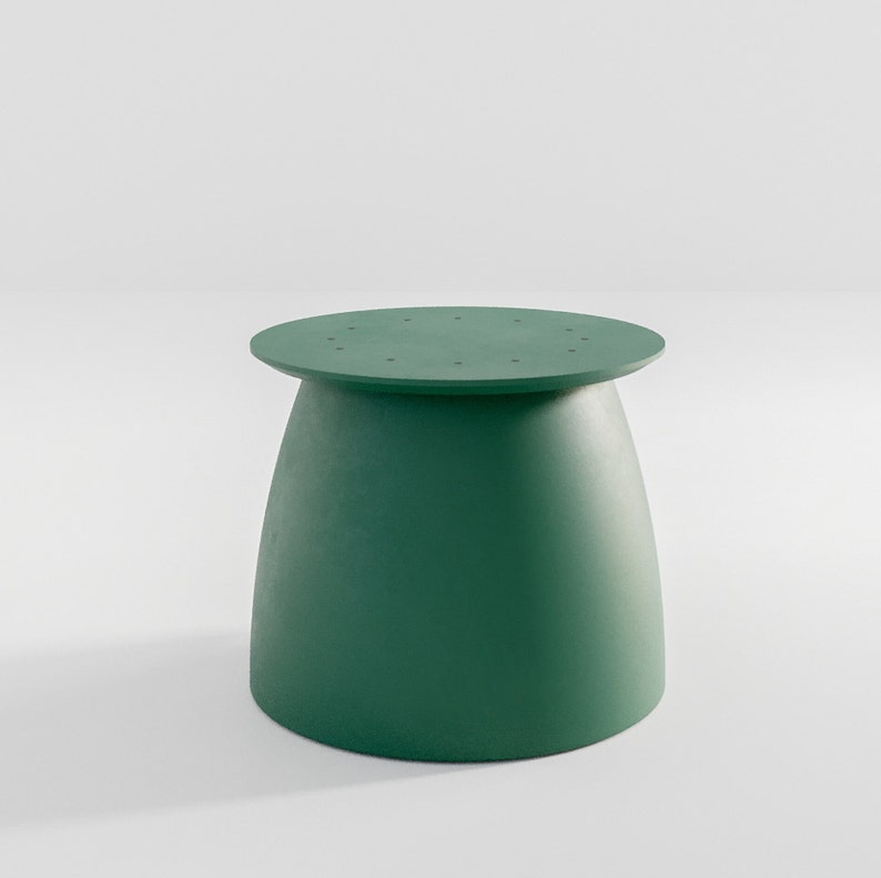 Pu&ograve; includere: Uno sgabello rotondo di colore verde con una base leggermente svasata. La parte superiore dello sgabello presenta un motivo circolare di piccoli fori.