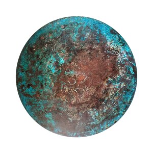 Op de afbeelding: Een rond metalen object met een getextureerde, verweerde afwerking. Het oppervlak toont een mix van bruine, turquoise en donkere tinten, wat een verouderde uitstraling geeft. De ronde vorm komt goed uit tegen een witte achtergrond.