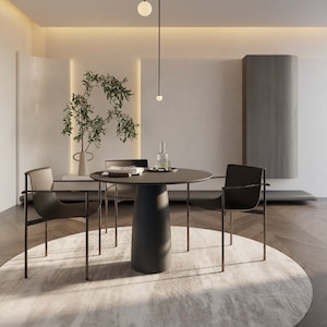 Può includere: Una moderna sala da pranzo con un tavolo rotondo grigio scuro e quattro sedie nere. Il tavolo ha una base a piedistallo e le sedie hanno sottili telai in metallo. Un grande tappeto colorato si trova sotto il tavolo. La stanza comprende un vaso di verde e un'illuminazione minimalista.