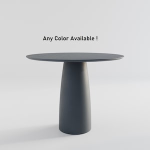 May include: A dark gray round table with a single, wide, cylindrical leg. The table is on a white background. Any Color Available!