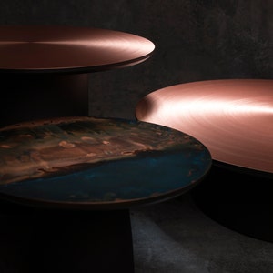 May include: Three round tables with different colored tops. The top table has a copper top, the middle table has a copper top, and the bottom table has a blue and brown top.