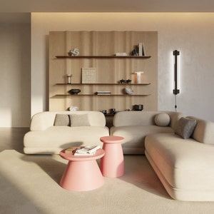 May include: A white sectional sofa with two pink side tables in a living room with a wooden shelf unit behind the sofa. The shelf unit has books, decorative objects, and a lamp on it.