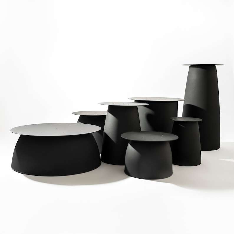 May include: A set of seven black metal tables of varying sizes and heights. The tables are all round and have a slightly curved top.