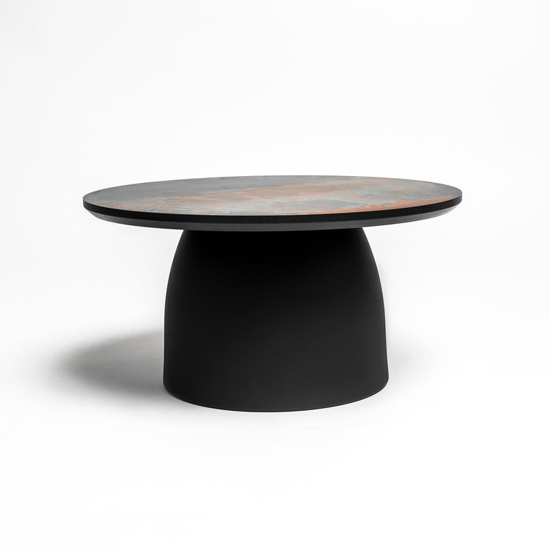 May include: A round, black coffee table with a unique, textured, gray and brown top. The table has a wide, round base.