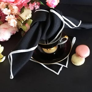 May include: A white ceramic mug with a black handle and the text "But First, Coffee" in a bold, black font. The mug is set against a blurred background, suggesting a cozy setting. The mug appears to be approximately 4 inches tall.