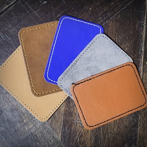 May include: Four leather wallet-sized card holders in different colors. The card holders are brown, blue, gray, and orange. The card holders are stitched with a decorative stitch.