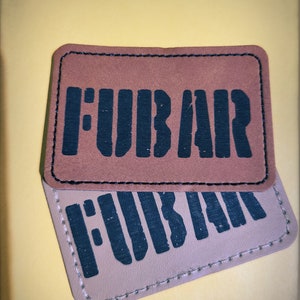 May include: Two brown leather patches with black stitching and the word "FUBAR" printed in black.