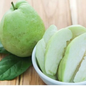 May include: A whole green guava and several slices of guava in a white bowl on a wooden surface.