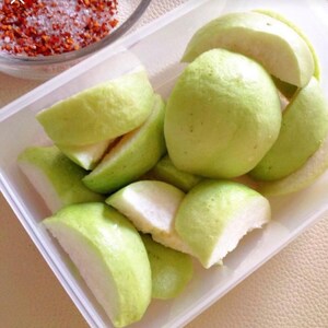 May include: A white plastic container filled with sliced green guava fruit. The guava is arranged in a circular pattern with the slices overlapping.