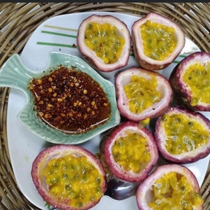 May include: A white plate with eight halved passion fruits, each with yellow flesh and black seeds. A small green dish shaped like a fish contains a red chili sauce.
