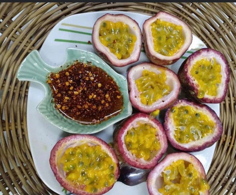 May include: A white plate with eight halved passion fruits, each with yellow flesh and black seeds. A small green dish shaped like a fish contains a red chili sauce.