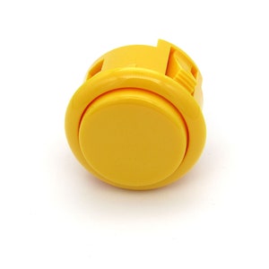 May include: A bright yellow arcade button with a rounded face and a rectangular base. The button is made of plastic and is designed for use in arcade games or similar applications. The button is shown against a white background.