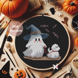Può includere: Un motivo a punto croce in un telaio di legno raffigura un fantasma con un cappello da strega che porta a spasso un cane, con pipistrelli sopra. Le parole "PDF Pattern" sono in un cerchio. Lo sfondo include zucche e decorazioni di Halloween.