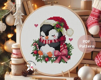 May include: A cross-stitch pattern of two penguins hugging, wearing a Santa hat and scarf, surrounded by a wreath and a pink bow. The design is in a wooden embroidery hoop, with the text "PDF Pattern" visible.