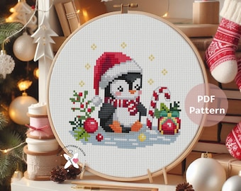 May include: A cross-stitch embroidery hoop featuring a Christmas penguin wearing a Santa hat and scarf. The penguin is surrounded by festive elements like a candy cane, gifts, and berries. The text "PDF Pattern" is visible.