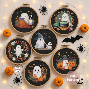 Może przedstawiać: Kolekcja wzorów do haftu krzyżykowego o tematyce Halloween w drewnianych tamborkach. Każdy z nich przedstawia uroczy wzór ducha z dyniami, nietoperzami i kapeluszami czarownic. Wzory są umieszczone na czarnym tle z elementami dekoracyjnymi.