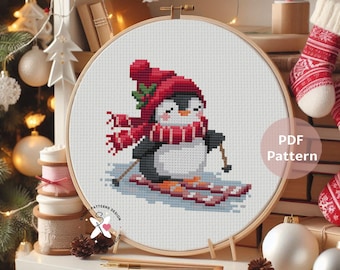May include: A cross-stitch pattern of a penguin skiing, wearing a red hat and scarf. The penguin is on skis, with a wooden embroidery hoop. The text "PDF Pattern" is visible.