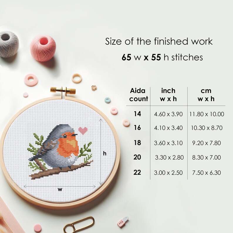 May include: A cross-stitch pattern of a robin bird with a red breast and a small heart on a branch. The pattern is shown in a wooden embroidery hoop with a white Aida cloth. The size of the finished work is 65 stitches wide by 55 stitches high. A table shows the finished size in inches and centimeters for different Aida counts.