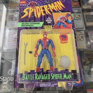 May include: Sealed Spider-Man action figure from the animated series, in original packaging. The figure is in a blue and red suit, with accessories. The packaging features the Spider-Man logo and the text "Battle Ravaged Spider-Man".