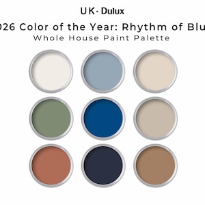 May include: Nine paint color samples in open metal containers. The colors include off-white, light blue, beige, olive green, deep blue, tan, terracotta, navy, and brown. Text at the top reads "UK-Dulux 2026 Color of the Year: Rhythm of Blues Whole House Paint Palette."
