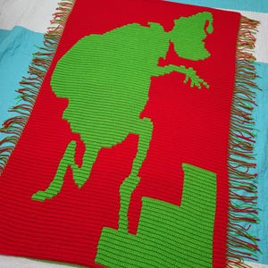 May include: A crocheted blanket with a green silhouette of the Grinch on a red background. The Grinch is standing on a green staircase.