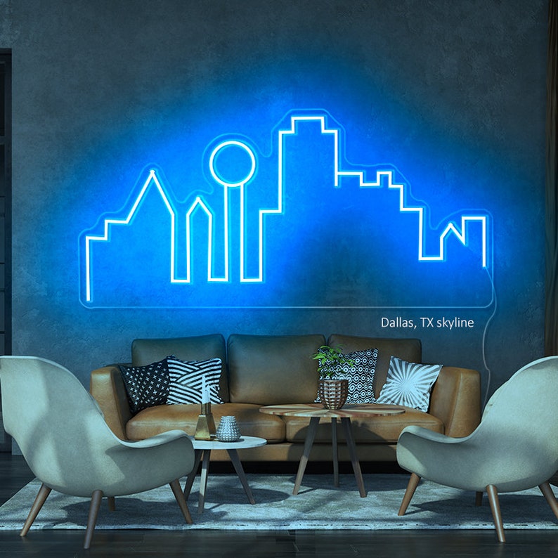 Pu&ograve; includere: Un'insegna al neon blu raffigurante lo skyline di Dallas, TX. L'insegna &egrave; montata su una parete grigio scuro sopra un divano in pelle marrone e due sedie di colore chiaro. Il testo "Dallas, TX skyline" &egrave; sotto.