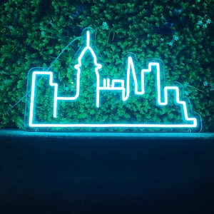 May include: A neon sign shaped like a city skyline, with a tall building in the center, against a green background.